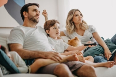 Family of four sitting on the couch watching TV at The Alery Fort Myers apartments istock 1331989704